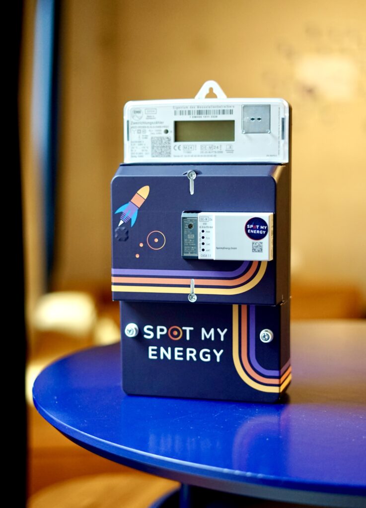 Close-up of a dark blue energy kiosk with a yellow rocket sticker and the text 'SPOT MY ENERGY' on the front, placed on a blue circular table.
