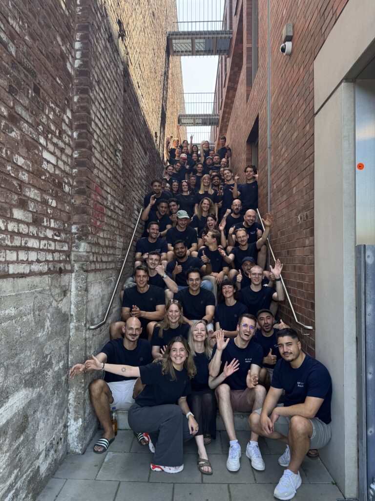 Group photo of about 40 people on a stairway between brick walls, many wearing navy shirts, waving and smiling at camera.