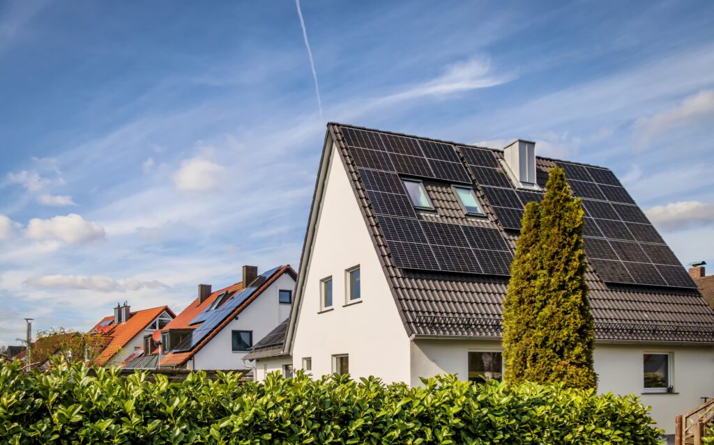 Row of white houses with dark tiled roofs covered in solar panels, under a blue sky with a faint contrail.